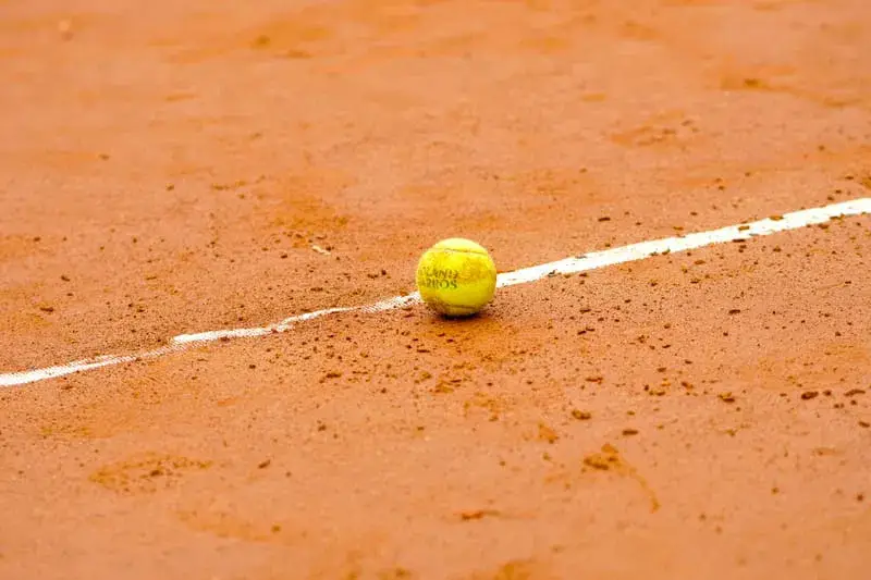 Balle de tennis jaune posée sur la ligne blanche d'un court en terre battue