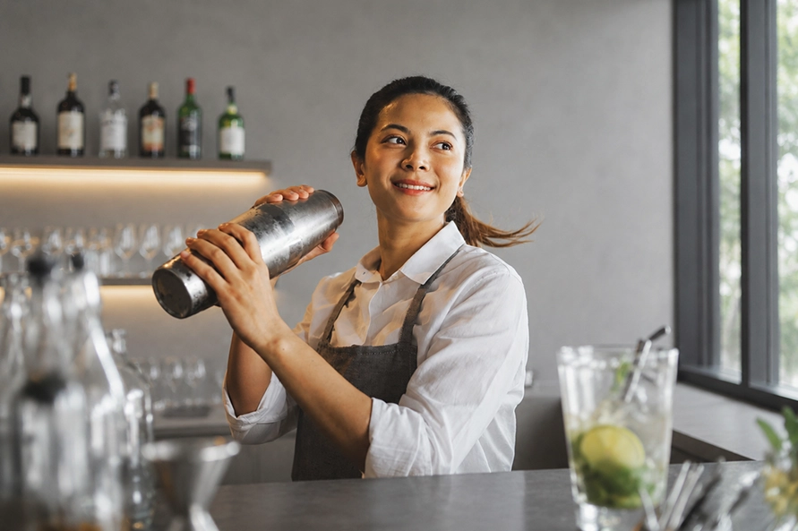 Barmaid souriante préparant un cocktail au shaker derrière un bar